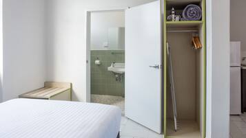 A hotel room with a bed, a small bedside table, a wardrobe with a mirror, and a bathroom visible through an open door.