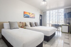 A hotel room with two beds, a desk, a chair, and a window with a geometric pattern. - Nightcap at Emerald Star Hotel (Emerald)