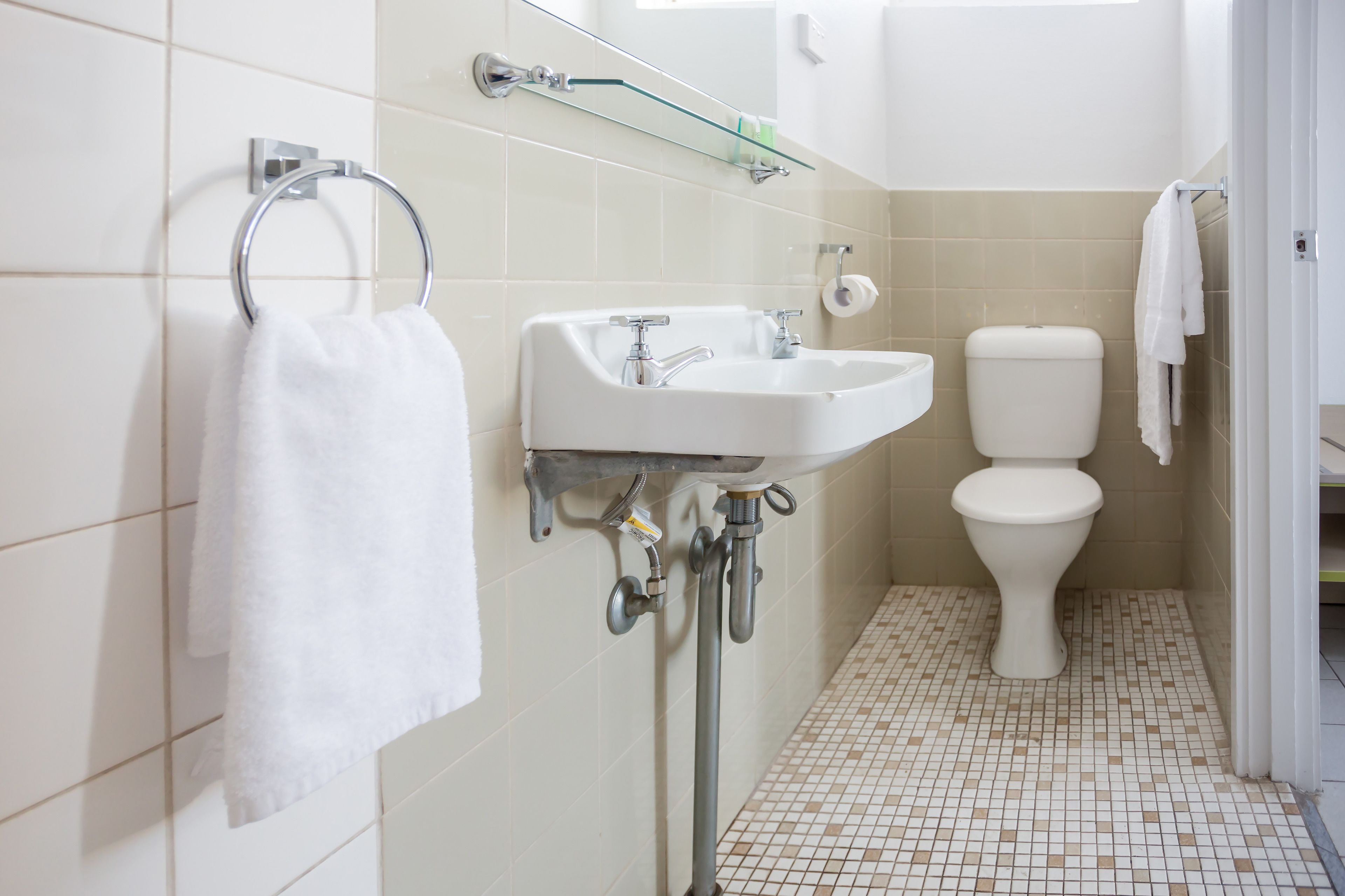 Un baño con lavamanos blanco, inodoro y estante de vidrio sobre el lavamanos.