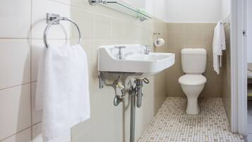 Un baño con lavamanos blanco, inodoro y estante de vidrio sobre el lavamanos.