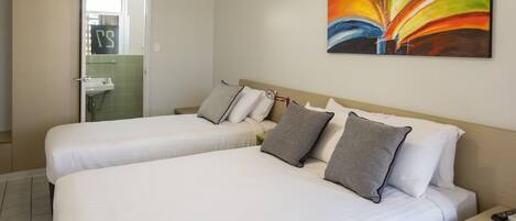 A hotel room with two beds, a bathroom, and a painting on the wall.