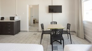 Habitación de hotel con cama, escritorio con microondas, televisor en la pared y zona de comedor con sillas.