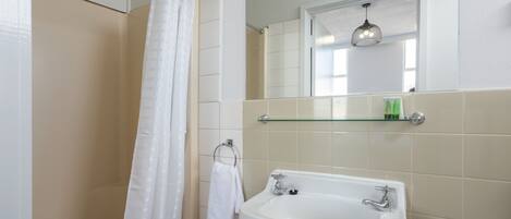 Un baño con ducha, un lavabo, un estante de vidrio con artículos de aseo y un espejo.