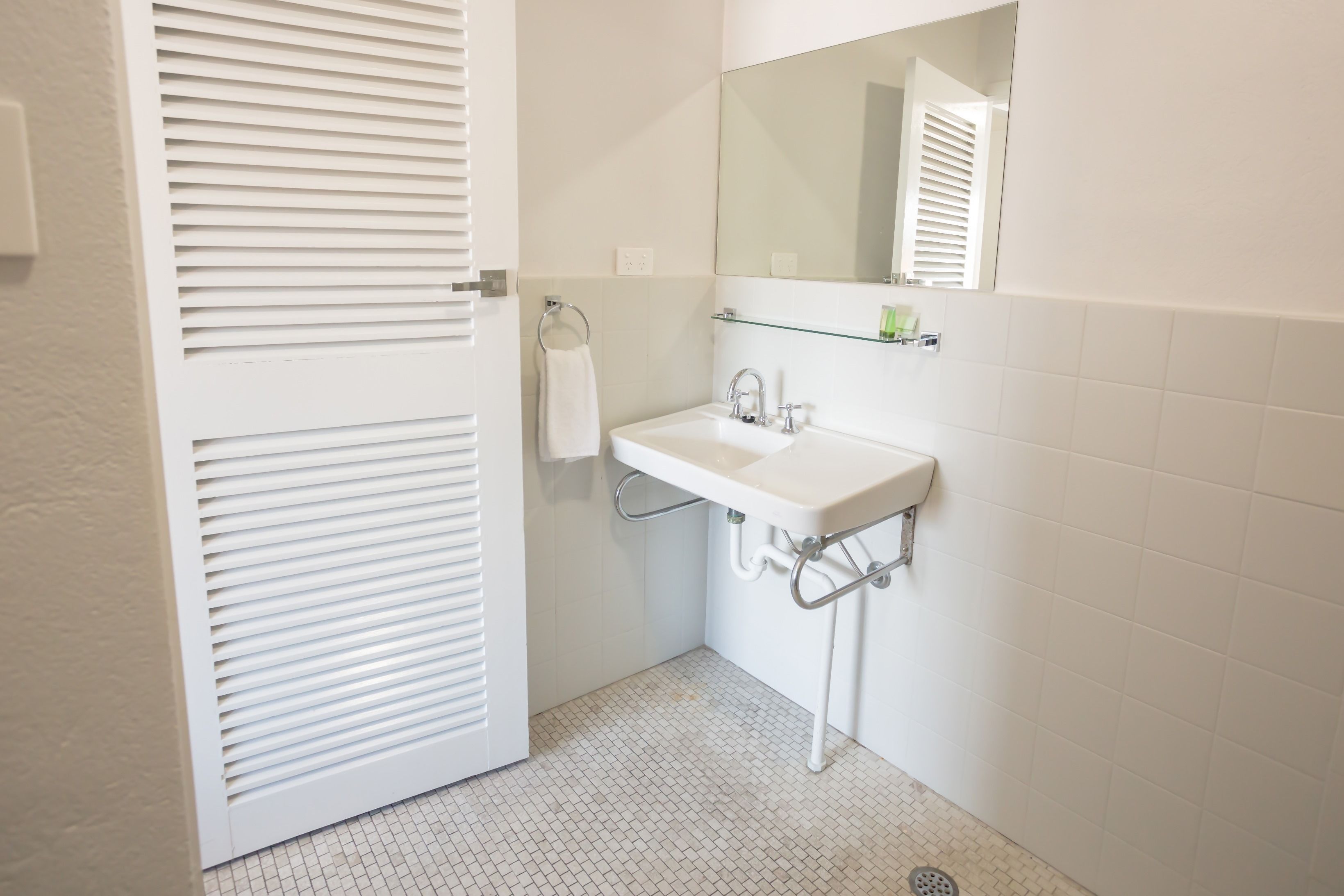 Un baño con lavamanos blanco, espejo y barra para toallas.