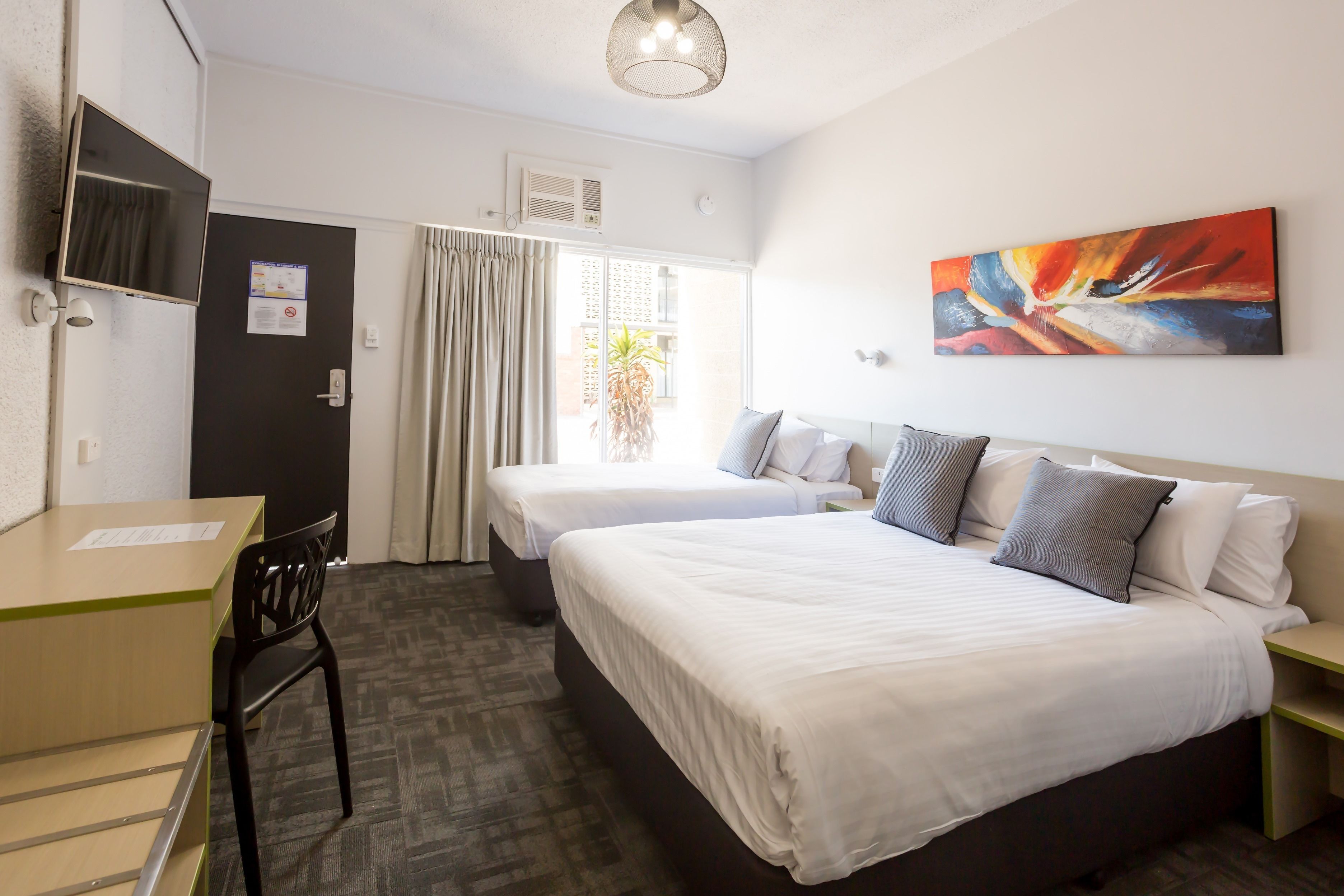 A hotel room with two beds, a desk, a chair, a TV, and a painting on the wall.