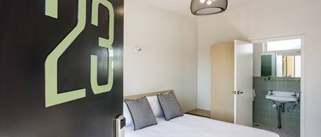 A hotel room with a bed, a door with a number, a bathroom with a sink, and a hanging light fixture.