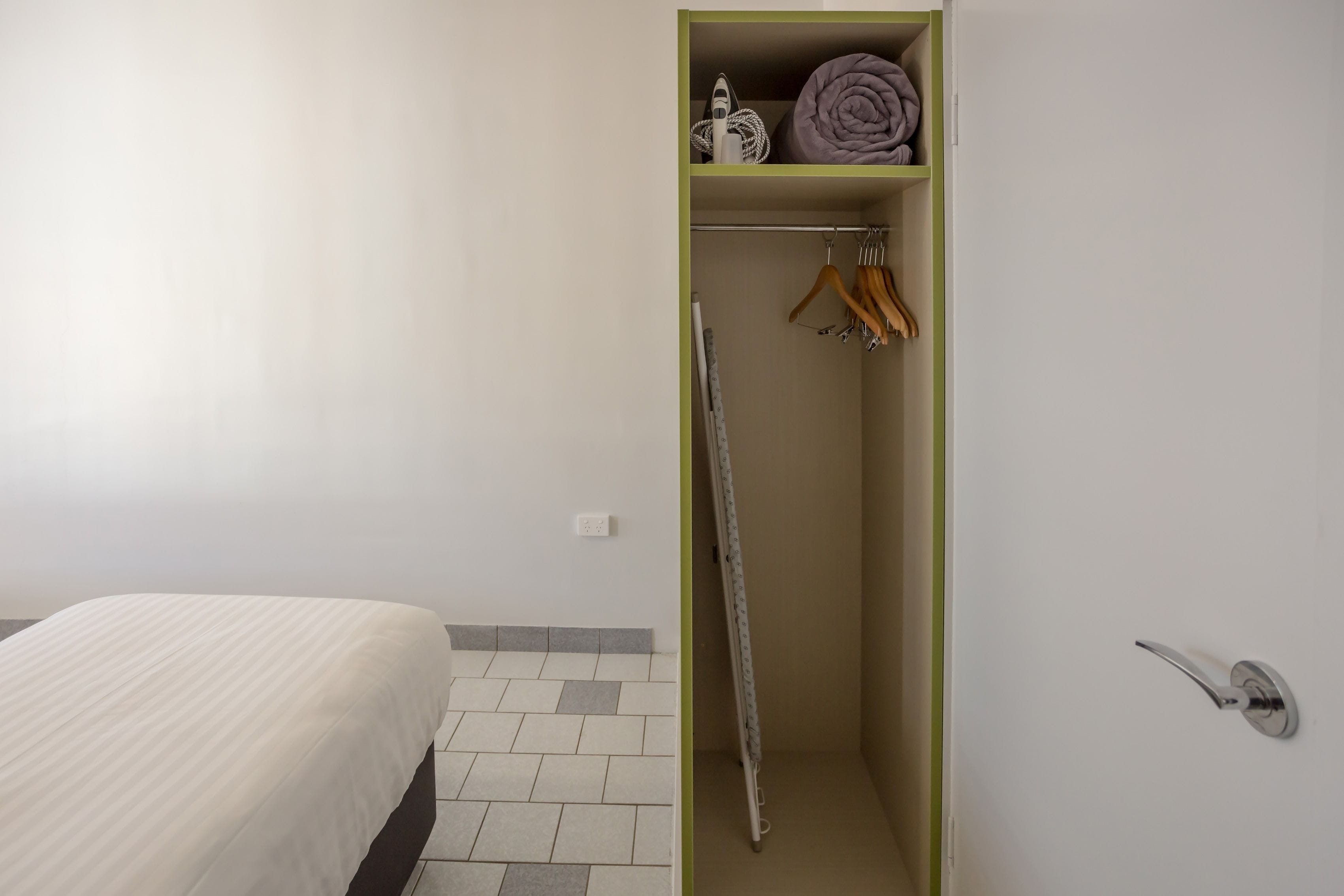 A bedroom with a bed, a wardrobe with hanging clothes, and a folded blanket on top.