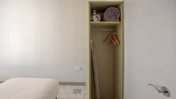A bedroom with a bed, a wardrobe with hanging clothes, and a folded blanket on top.