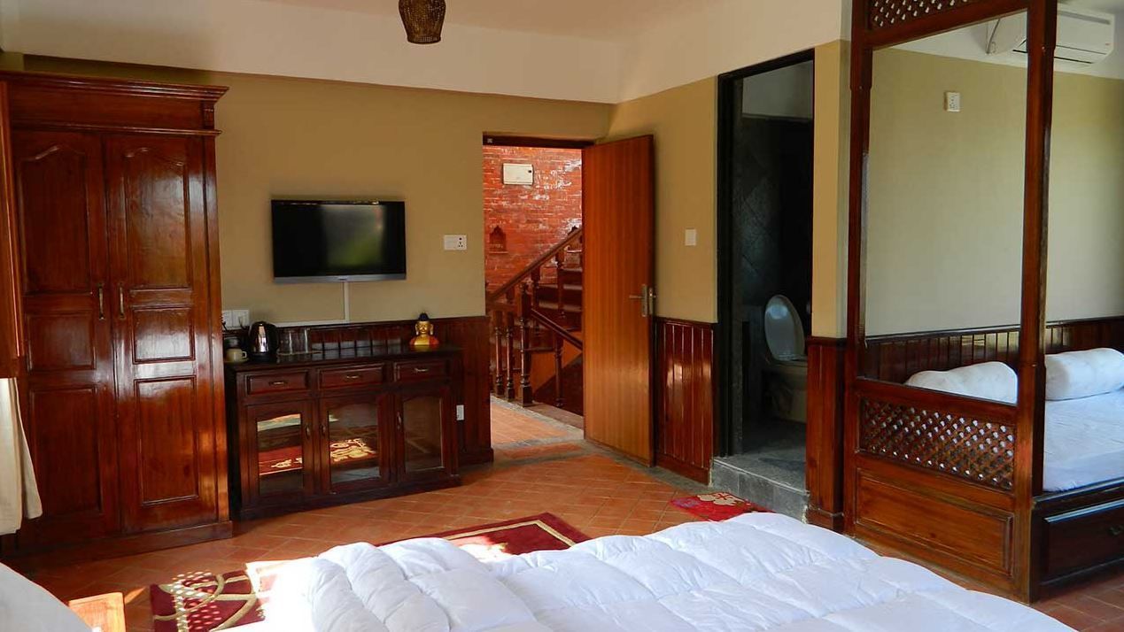 A hotel room with a large bed, wooden furniture, a television, and a staircase leading to another room.