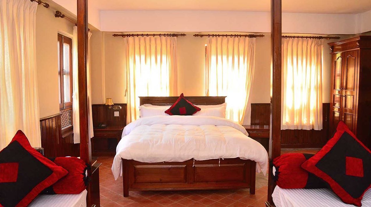 Una cama con dosel con ropa blanca y almohadas rojas y negras, flanqueada por cortinas y un armario de madera.
