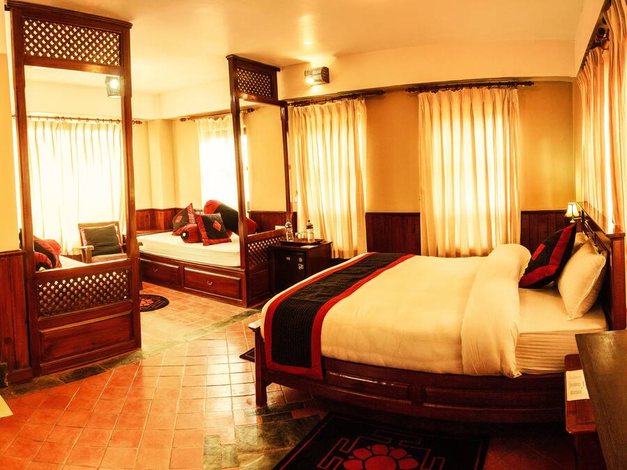 Une chambre d’hôtel avec un grand lit, une tête de lit en bois, une table de chevet, un miroir et une fenêtre avec des rideaux.