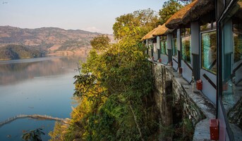 Un hotel con techo de paja, con vistas a un lago tranquilo y rodeado de exuberante vegetación.