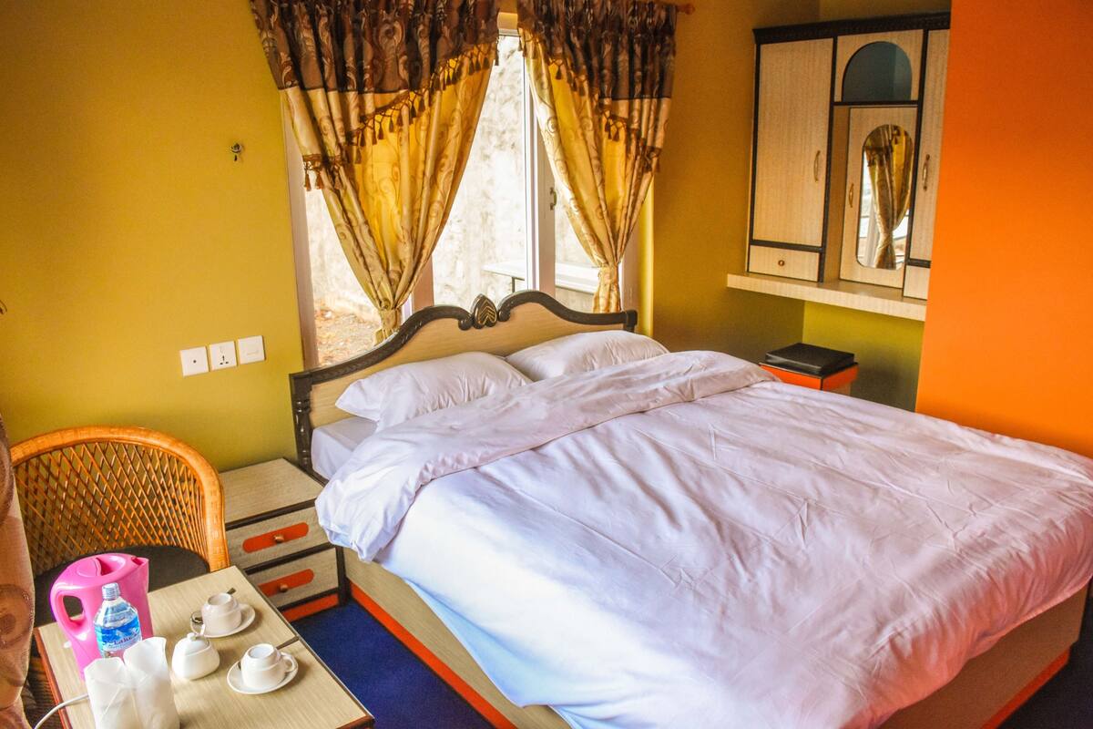 Quarto de hotel com cama, mesa com chá, uma cadeira e janela com cortinas.