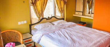 A hotel room with a bed, a table with tea set, a chair, and a window with curtains.