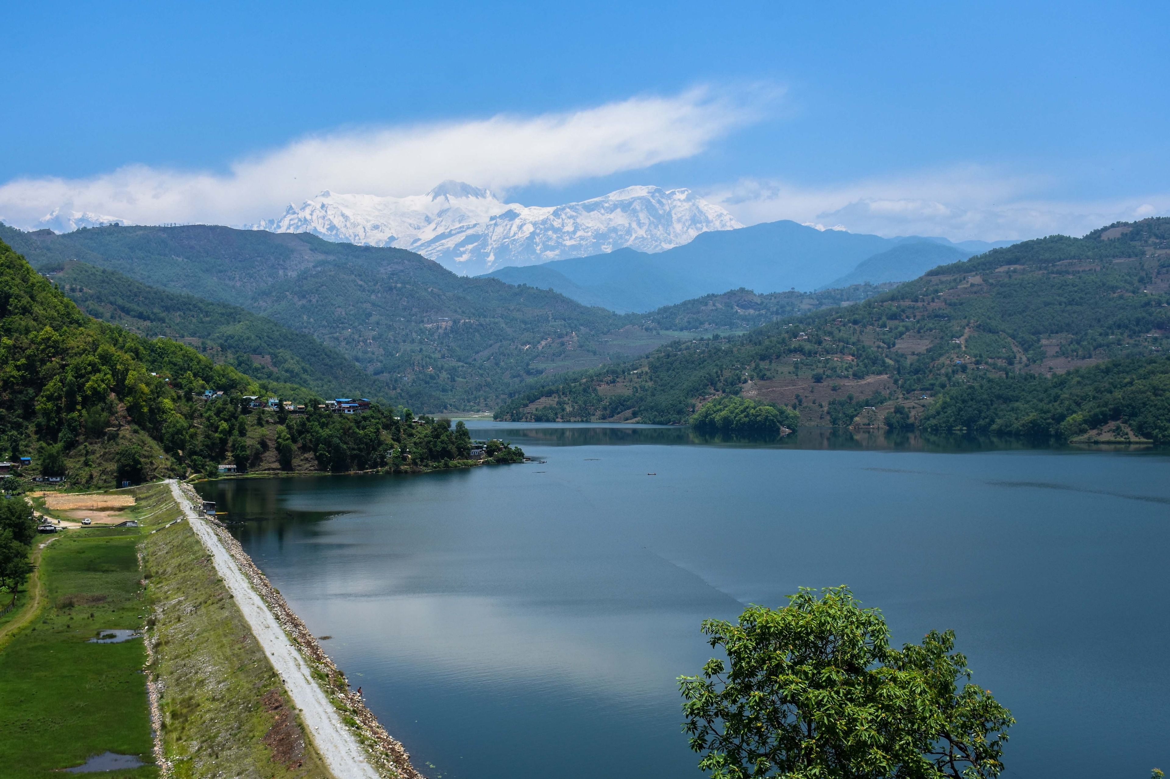 A serene lake surrounded by lush green hills and snow-capped mountains in the background.