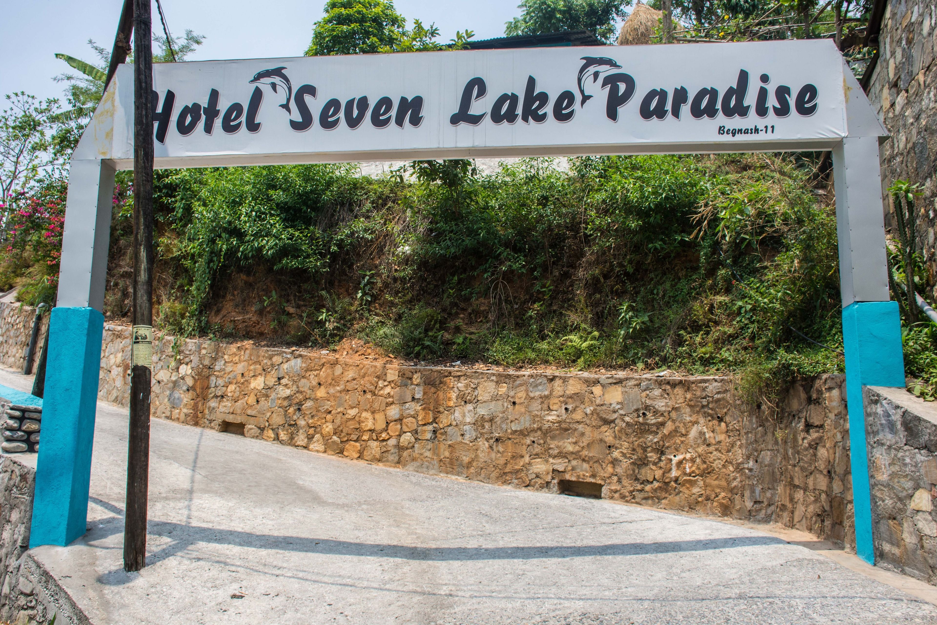 A sign for Hotel Seven Lake Paradise with a stone wall and greenery in the background.