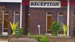 A reception area with a sign, brick walls, and potted plants. - Regency Hotel Fairmile (Gweru)