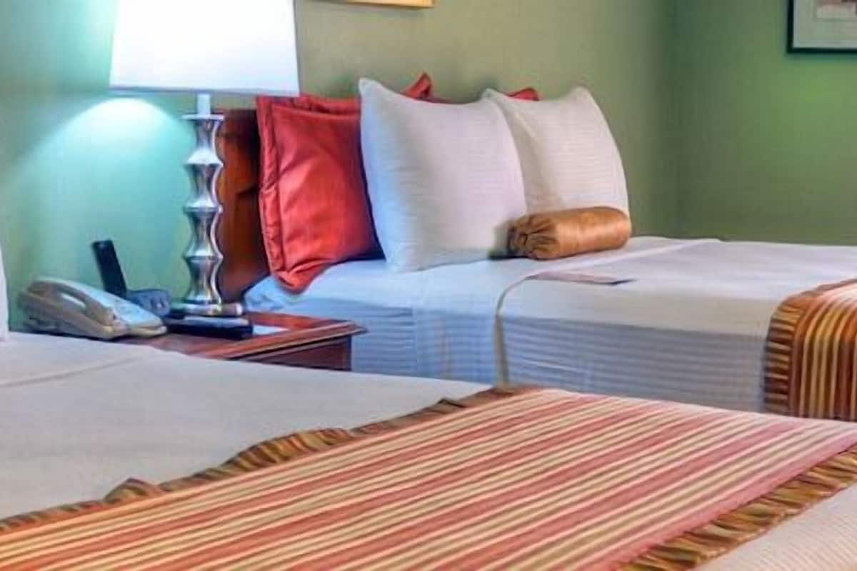 A hotel room with two beds, a nightstand, a lamp, and a telephone.