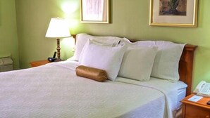 A neatly made bed with white linens and a brown throw pillow in a room with green walls and a framed picture above the bed. - Regency Hotel Fairmile (Gweru)