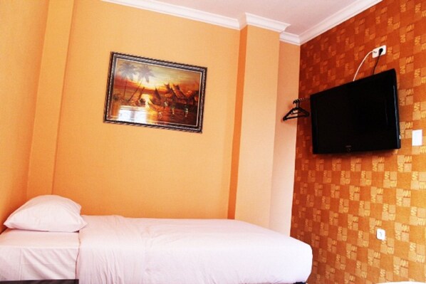 A hotel room with a bed, a painting on the wall, and a TV mounted on the wall.