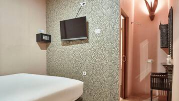 Une chambre à coucher comprenant un lit, un téléviseur fixé au mur, un petit coffre-fort et une porte donnant sur une autre pièce.