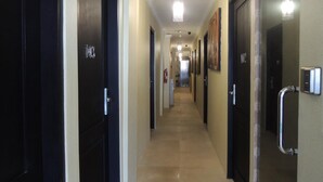 Un couloir d’hôtel avec des portes noires numérotées 103 et 102, un extincteur et une main courante sur le mur de droite.