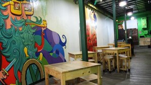 L’intérieur d’un restaurant est agrémenté de tables et de chaises en bois, d’une fresque colorée sur le mur et d’un plafond vert.