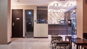 Un hall d’hôtel comprenant un comptoir d’accueil, une entrée avec une porte en verre et un espace détente avec des meubles en bois.