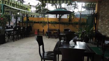 Un patio al aire libre con mesas y sillas, rodeado de plantas y un muro amarillo.