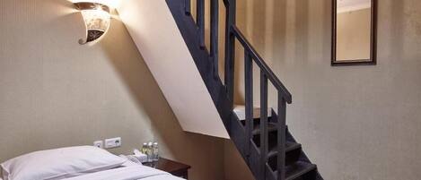 Una habitación de hotel con una cama, una mesita de noche, un teléfono, una botella, un espejo y una escalera.