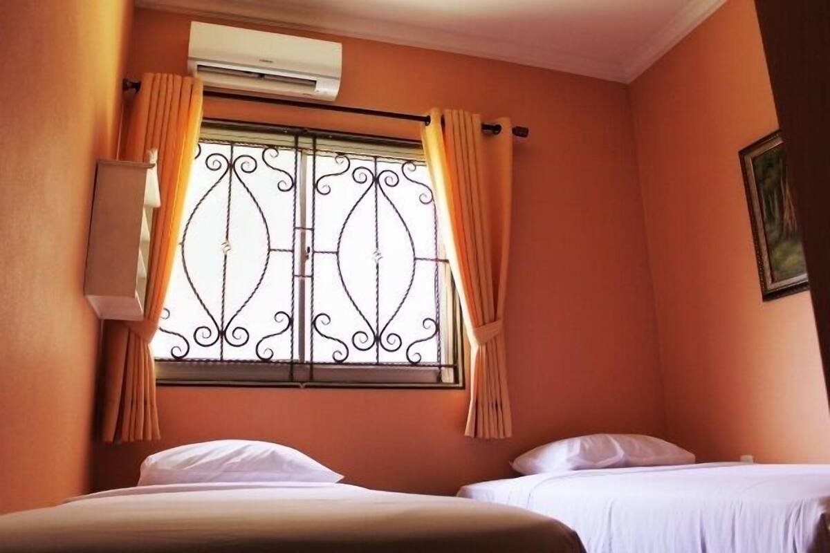 Ein Hotelzimmer mit zwei Betten, einer Klimaanlage, einem Fenster mit dekorativen Eisengittern und Vorhängen.