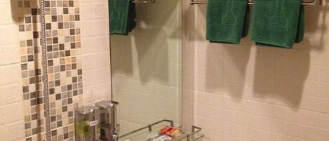 A bathroom with a shower, a sink, a mirror, and a towel rack with green towels.