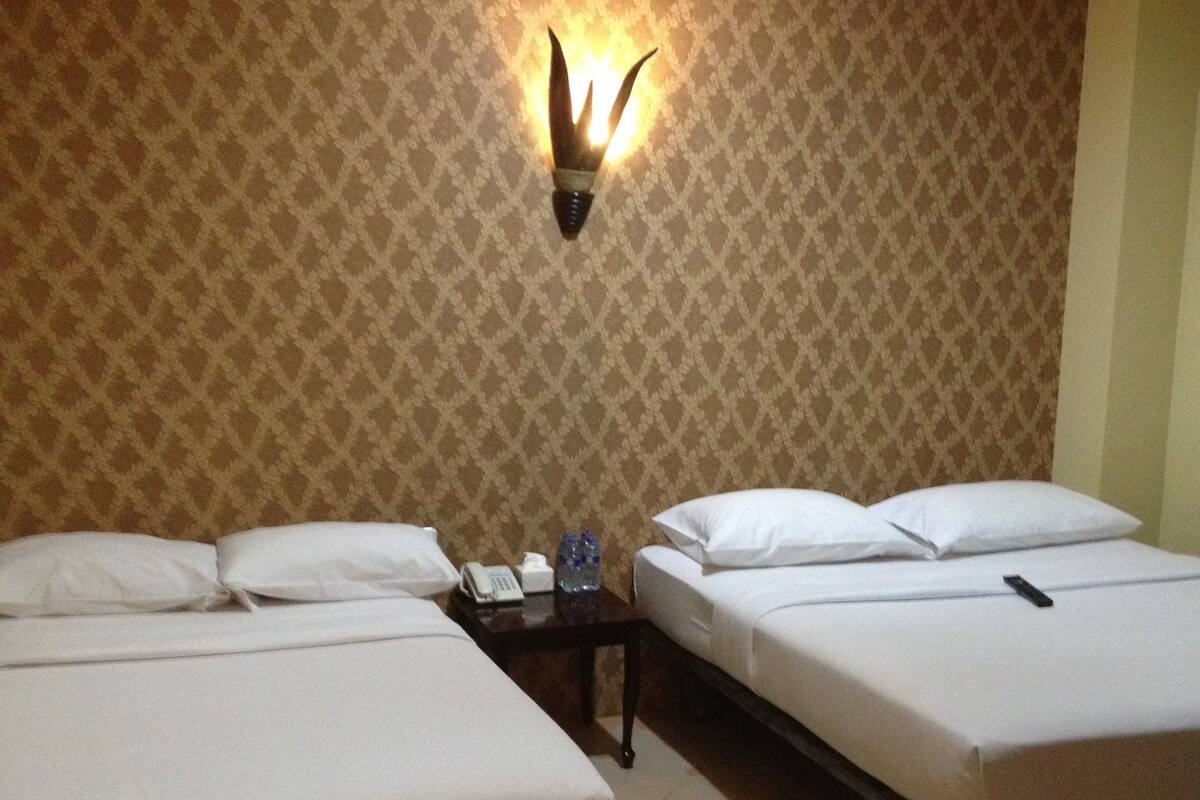 Ein Hotelzimmer mit zwei Betten, einem Nachttisch, einer Wandlampe und einem gemusterten Wandteppich.
