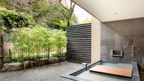 Un espace de détente extérieur moderne, comprenant un bain à remous en pierre, un banc en bois et un jardin de bambous.