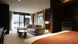 Une chambre d’hôtel avec un grand lit, un canapé, une petite table et un téléviseur. Elle dispose d’un balcon avec vue sur les arbres et une rambarde.
