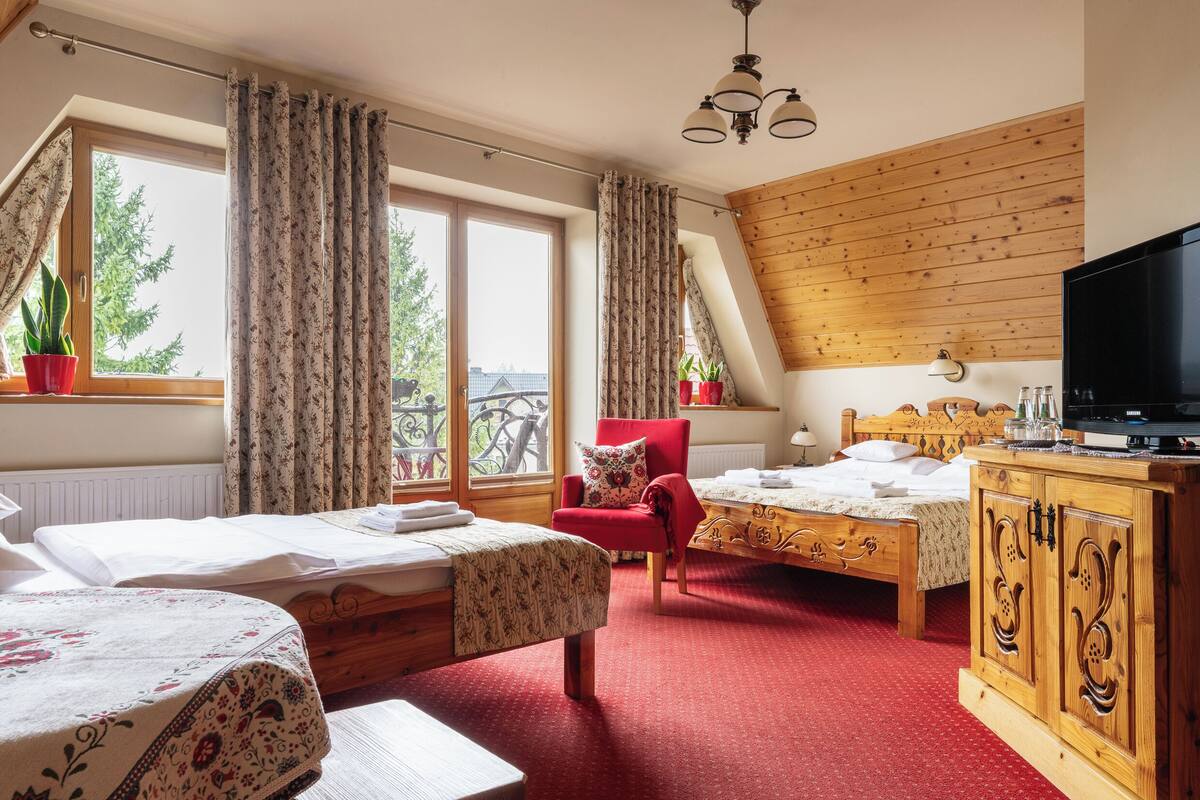 A room with two beds, a red armchair, a wooden cabinet, and a television.