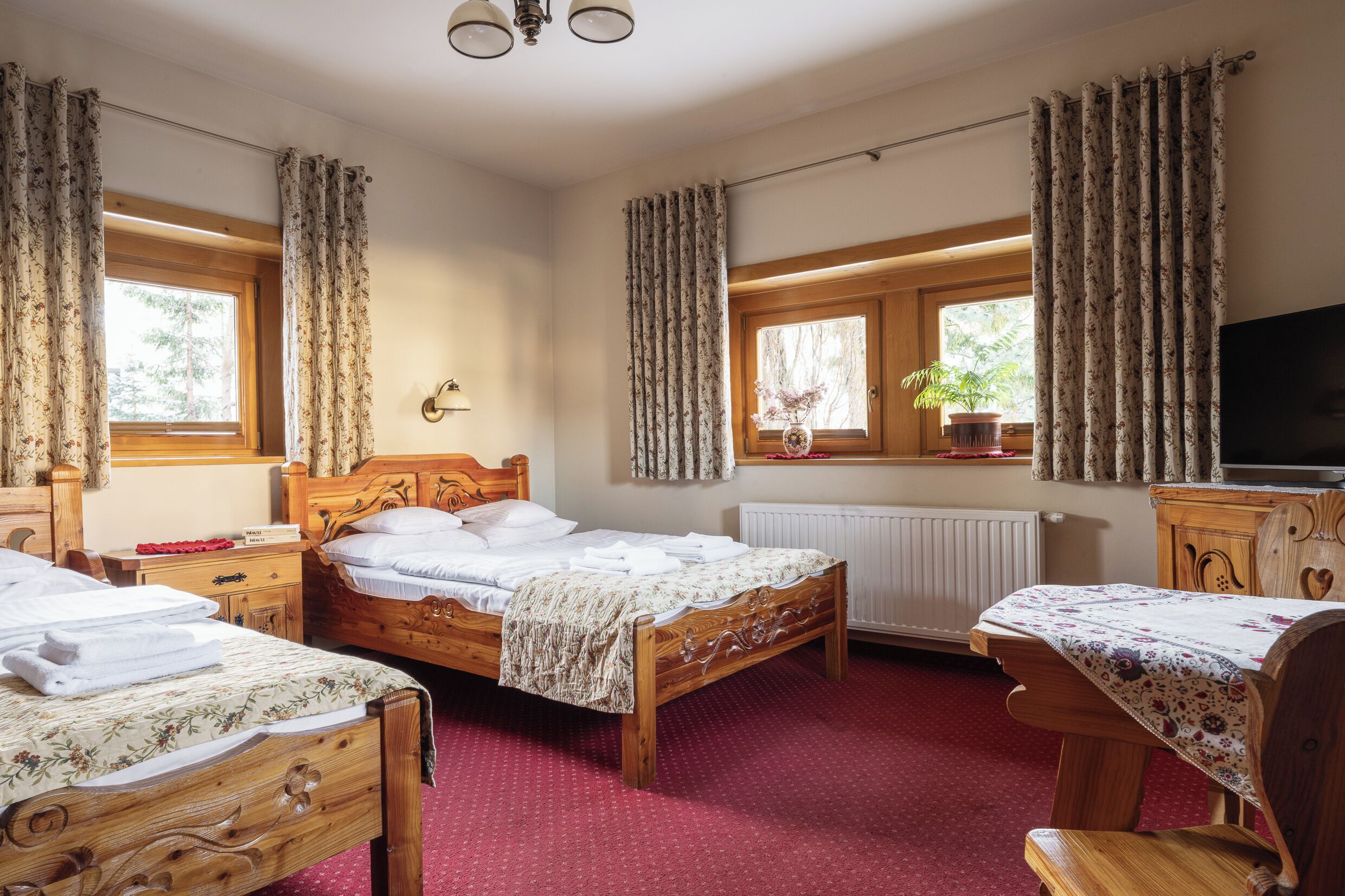 Une chambre à coucher avec deux lits en bois, une commode en bois, un téléviseur et une fenêtre avec des rideaux.
