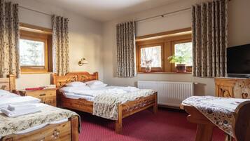 Une chambre à coucher avec deux lits en bois, une commode en bois, un téléviseur et une fenêtre avec des rideaux.