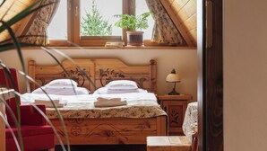Un dormitorio con una cama de madera, una mesita de noche con lámpara, un ventanal con vistas a árboles y una silla roja.