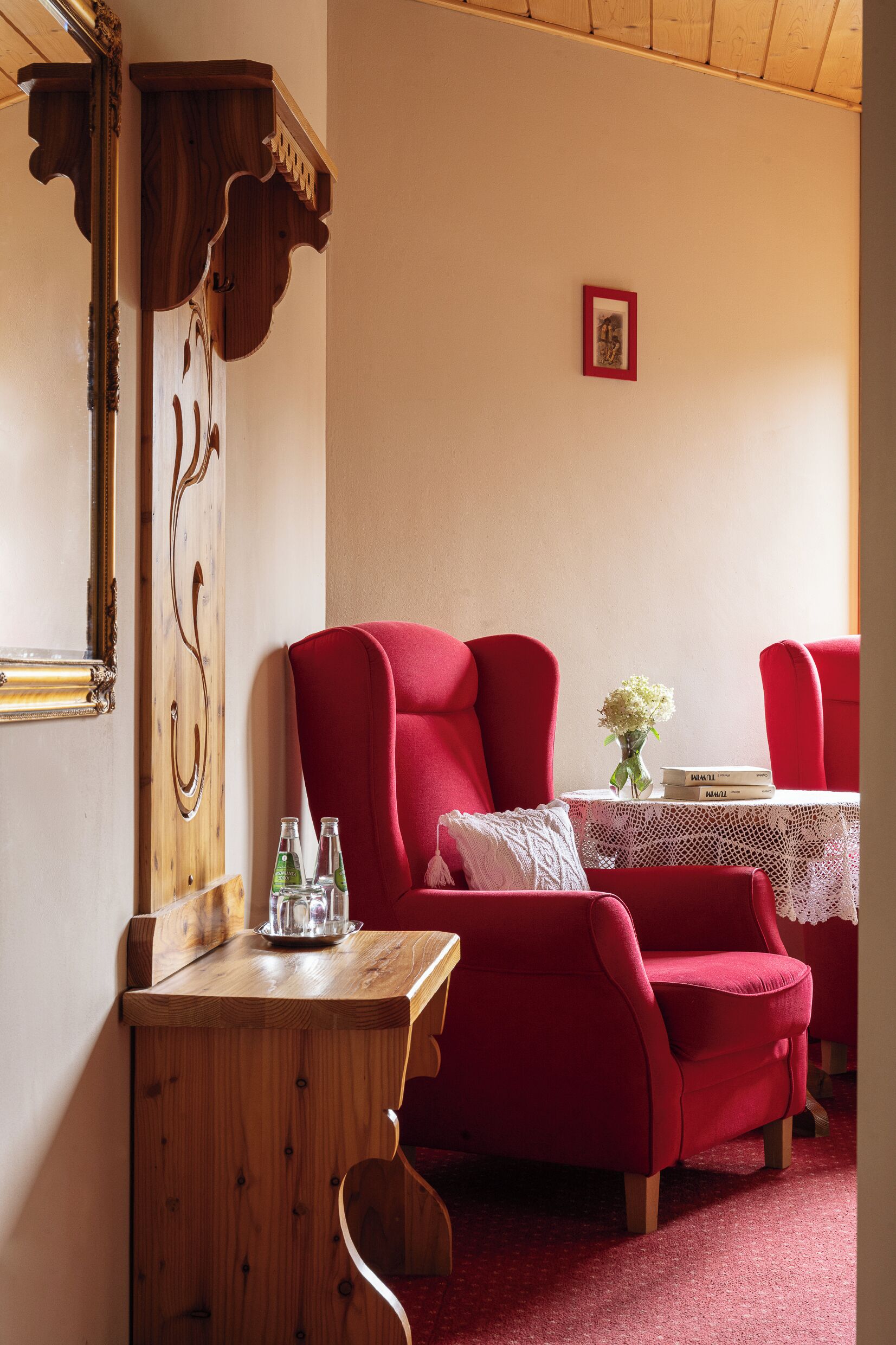 Una habitación con una mesa de madera, sillas rojas, un mantel de encaje blanco y un pequeño jarrón con flores.