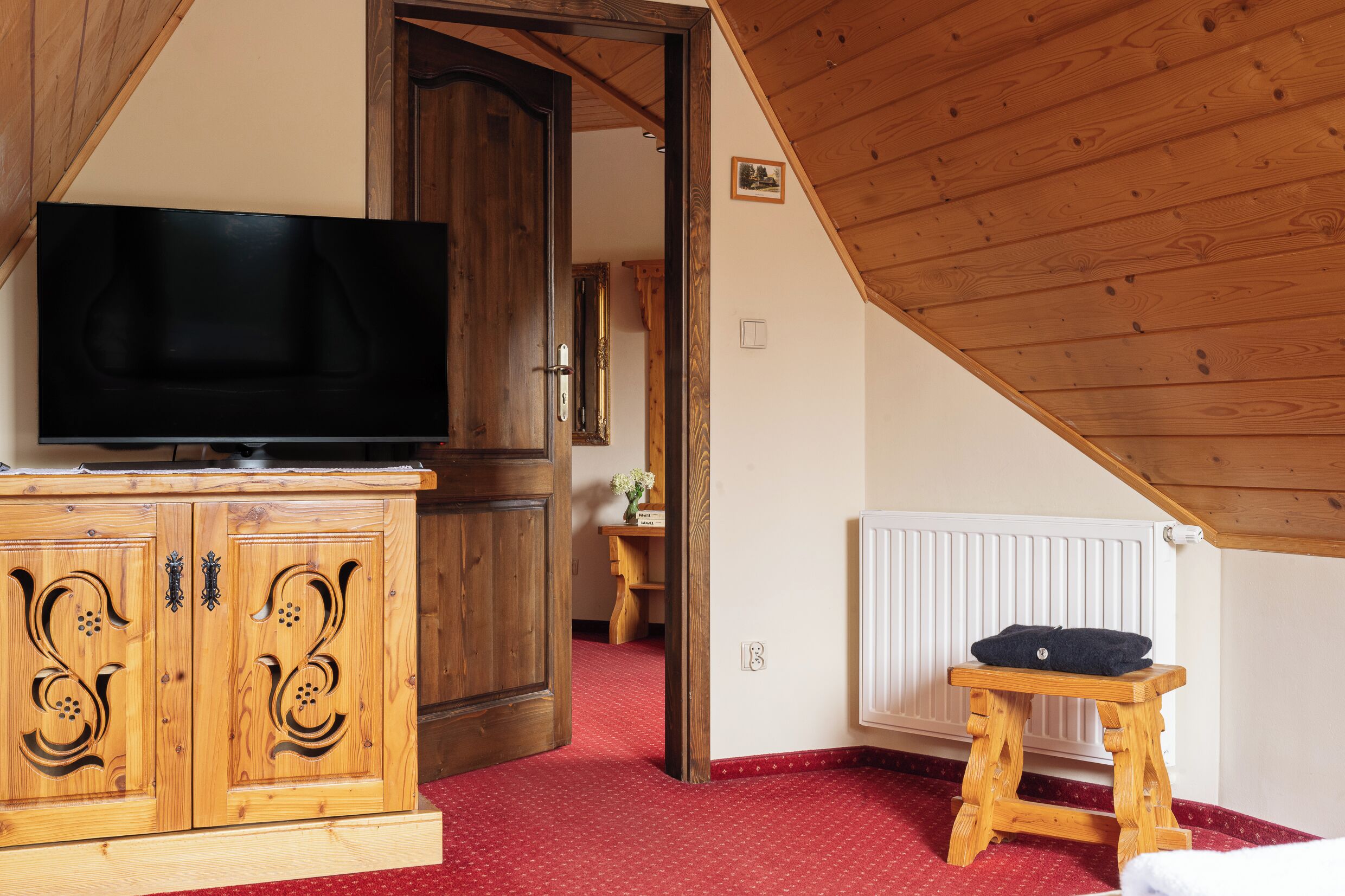 A room with a wooden cabinet, a television, a radiator, and a small stool.