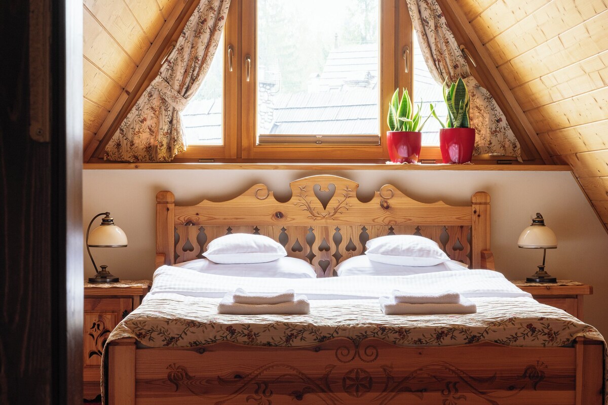 A wooden bed with a decorative headboard, two bedside lamps, and a window with curtains.