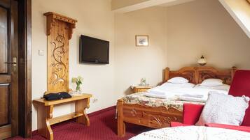 A bedroom with a wooden bed, a red chair, a wooden desk, a television, and a small bedside table.