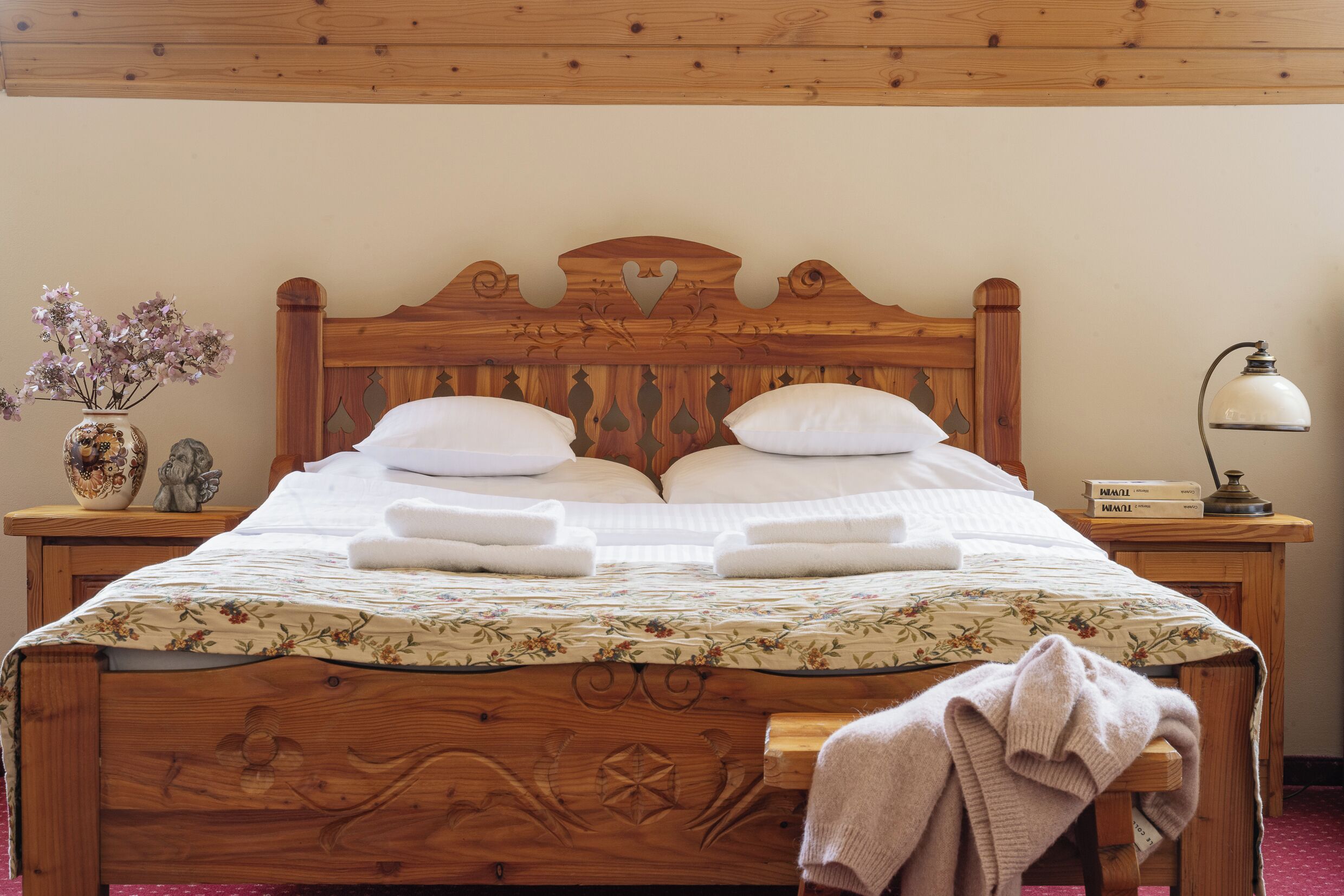 Una cama de madera con colcha estampada, dos almohadas y una mesita de noche con lámpara y un florero.