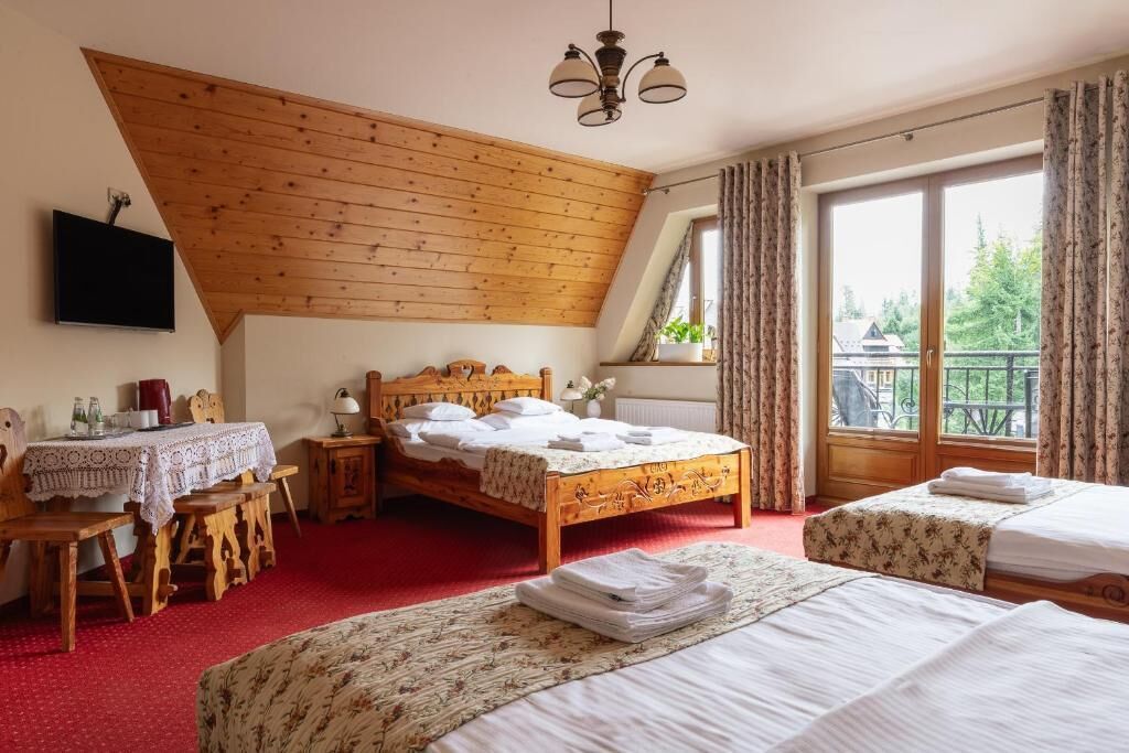 A bedroom with a wooden ceiling, a large bed, a smaller bed, a desk with a table, and a window with curtains.