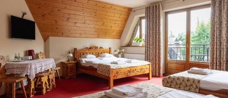 A bedroom with a wooden ceiling, a large bed, a smaller bed, a desk with a table, and a window with curtains.