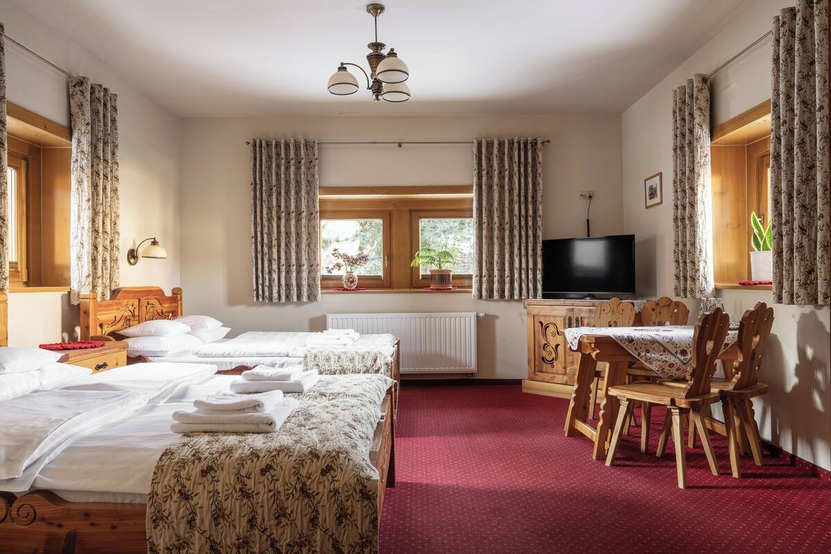 A hotel room with two beds, a dining table with chairs, a TV, and a window with curtains.