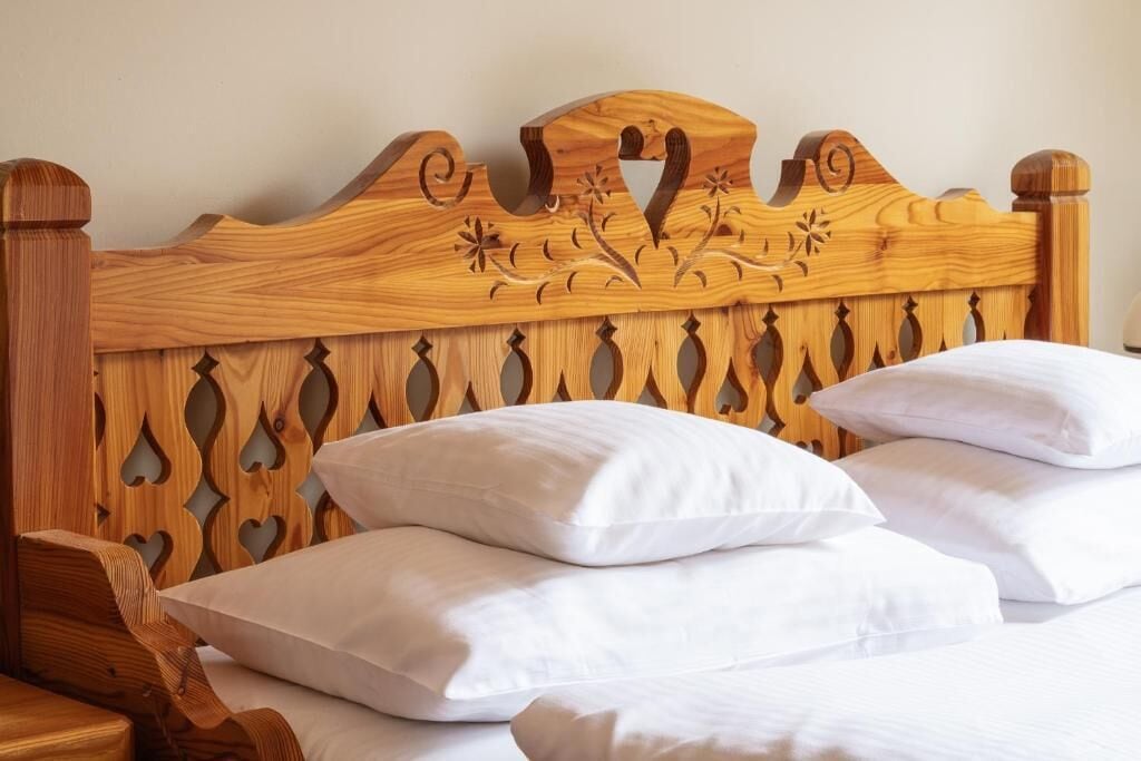 A wooden headboard with carved floral designs and heart-shaped cutouts, accompanied by white pillows.