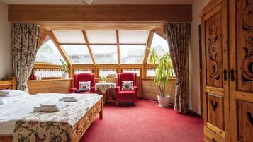 A cozy room with a bed, two red armchairs, a small table with a plant, and a large wooden wardrobe.