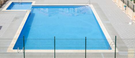 Uma piscina retangular grande com um calçadão ao redor e uma cerca.